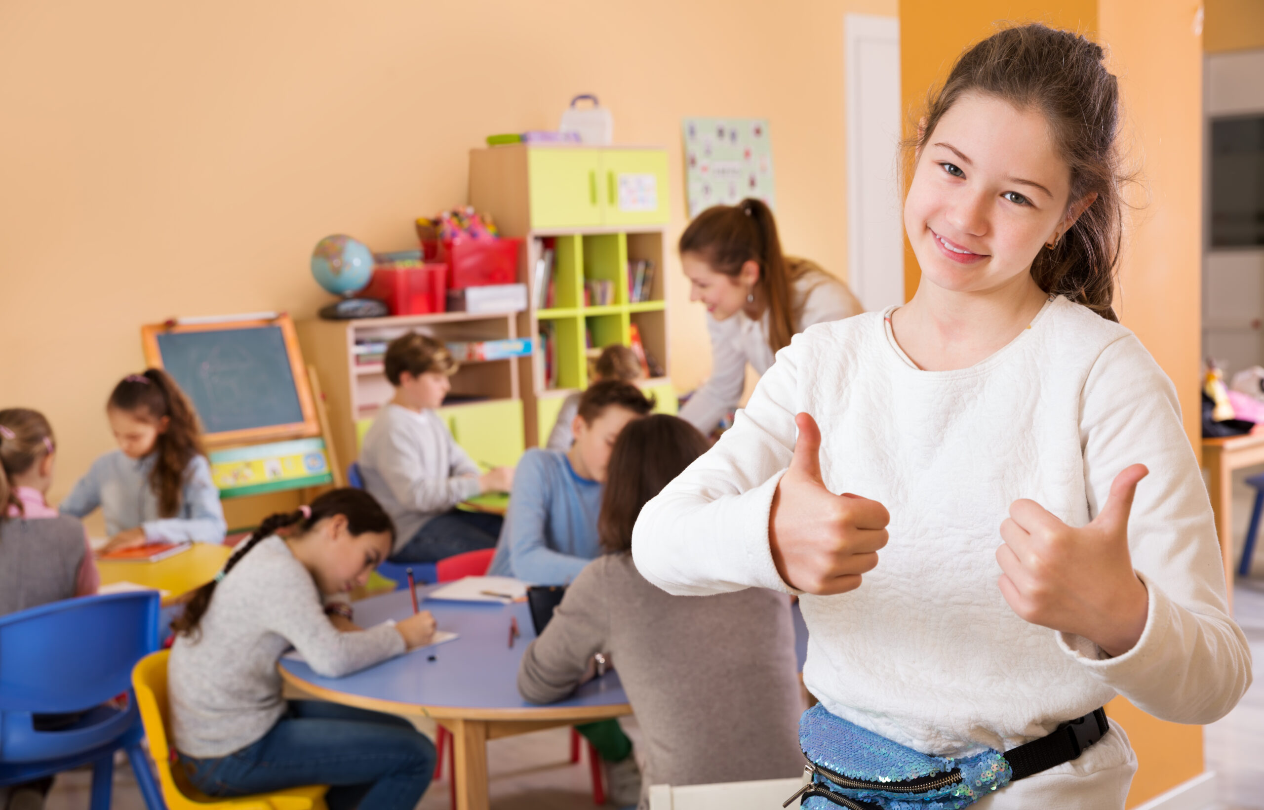 Portrait,Of,Happy,Schoolgirl,Standing,Foreground,In,The,Classroom,With